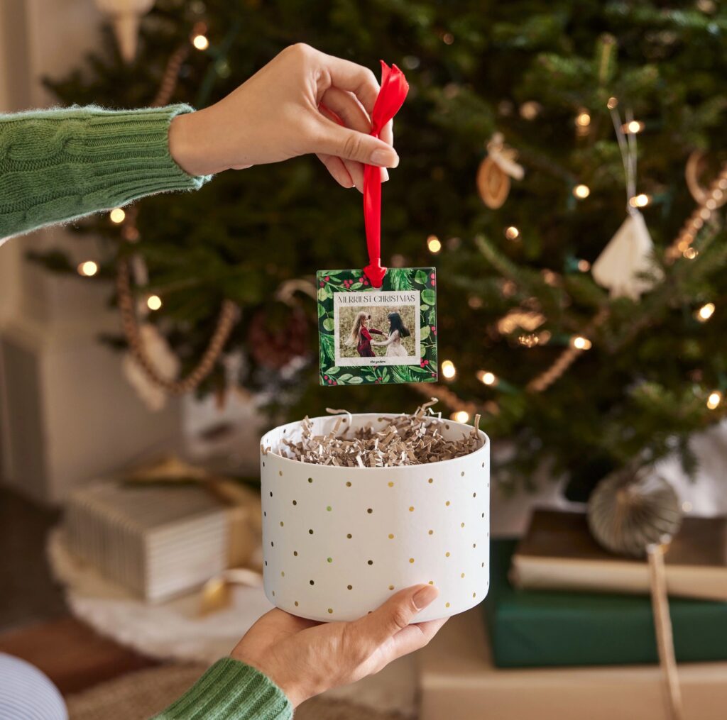 woman holding a photo christmas ornament above a mug with a christmas tree in the background