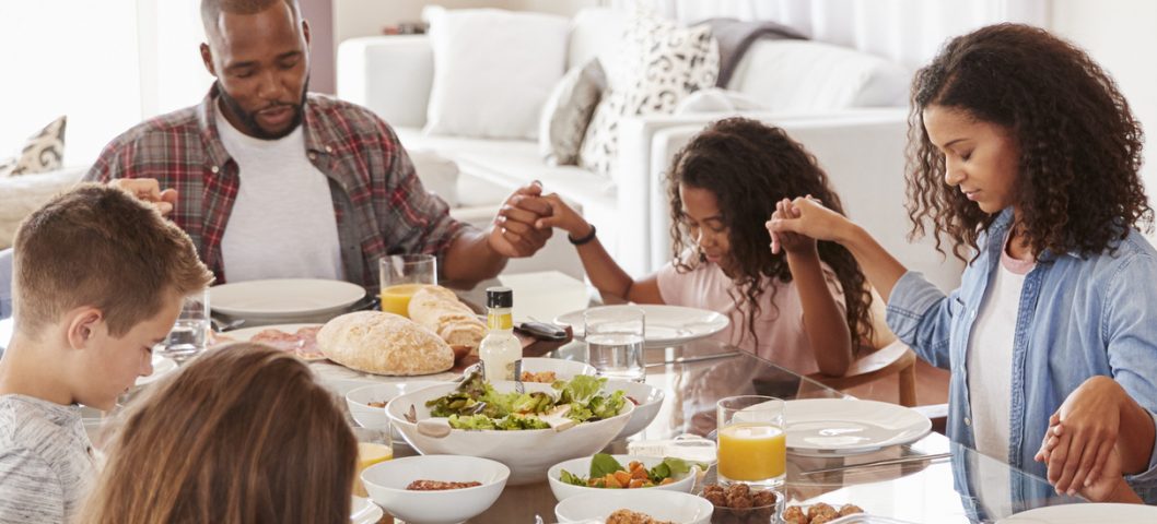 Two Families Praying Before Enjoying Meal At Home Together.