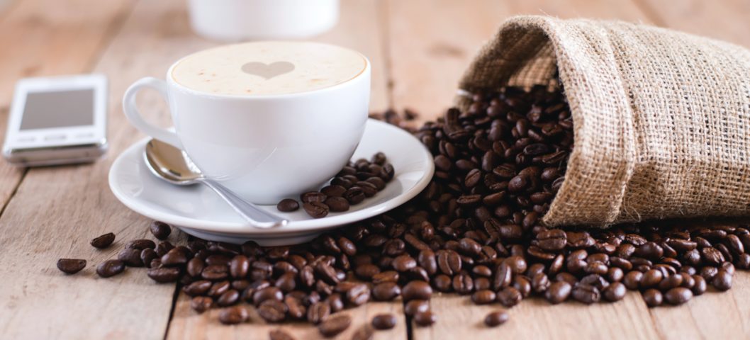 Bag of coffee beans spills next to cup of coffee